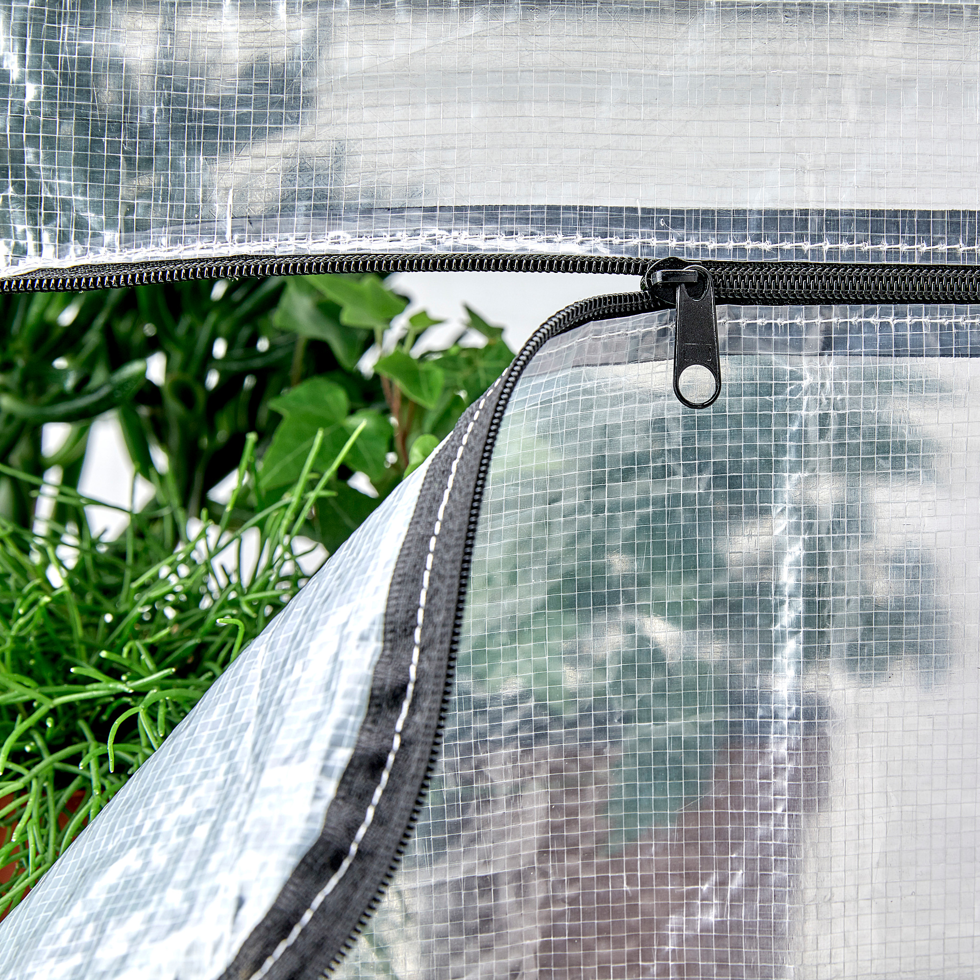 Primeiro plano dunha cuberta de polietileno transparente con cremalleiras e ganchos de nylon, protexendo as plantas verdes dentro dunha unidade de estantes.
