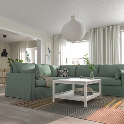 Sala de estar con sofá seccional HYLTARP, alfombra, mesa de café e cortinas.