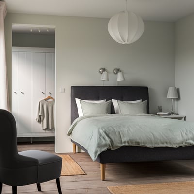 Dormitorio moderno con cama IDANÄS, luz pendente, cadeira negra, armario branco e alfombras lixeiras.