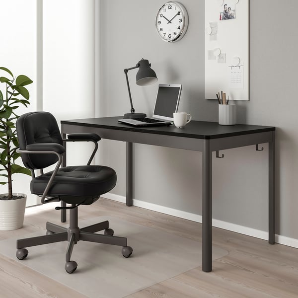 Moderna configuración de oficina negra compacta. Escritorio con portátil, cadeira, lámpada e planta. Reloxo e notas na parede.