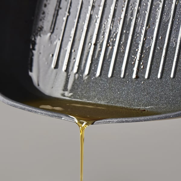 Primeiro plano de aceite dourado pingando da tixola antiadherente.