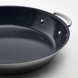 Primeiro plano de tixola antiadherente de alta calidade con dobres mangos de aceiro inoxidable, mostrando unha superficie interior lisa e escura e unha construción robusta.