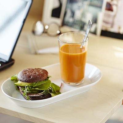 Unha comida cun bocadillo recheo de verduras e un vaso de zume de laranxa nun prato branco.
