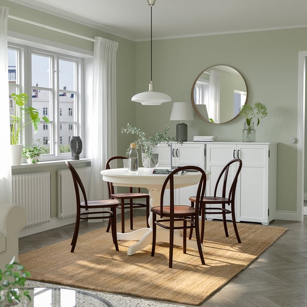 Comedor acolledor con mesa extensible INGATORP e cadeiras de madeira escura nunha alfombra de xute, colocada contra paredes verdes con luz natural.