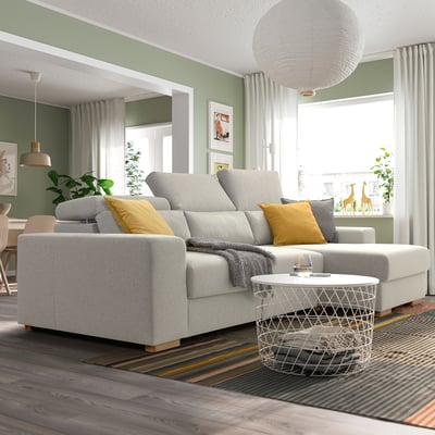 Sala de estar moderna con gran sofá seccional gris ISTABY, almofadas amarelas, mesa de café branca, alfombra de raias, xanela grande e plantas.