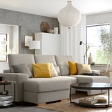 Sala de estar moderna con sofá seccional gris ISTABY, grandes almofadas amarelas, mesa de café de vidro, xanela grande, lámpada de chan e luz colgante branca.