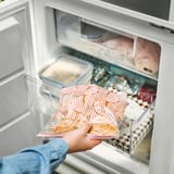 Persoa que sostén unha bolsa de conxelador reutilizable e transparente cun patrón colorido, que contén alimentos conxelados, extraídos dun conxelador.