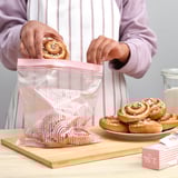 A persoa coloca a pastelería nunha bolsa reutilizable de ikea ISTAD sobre taboleiro de madeira, mostrando a súa fresca conservación e organización.