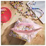 Bolsas de almacenamento vermellas e translúcidas cheas de perlas coloridas nunha mesa de madeira, xunto con táboas de perlas.