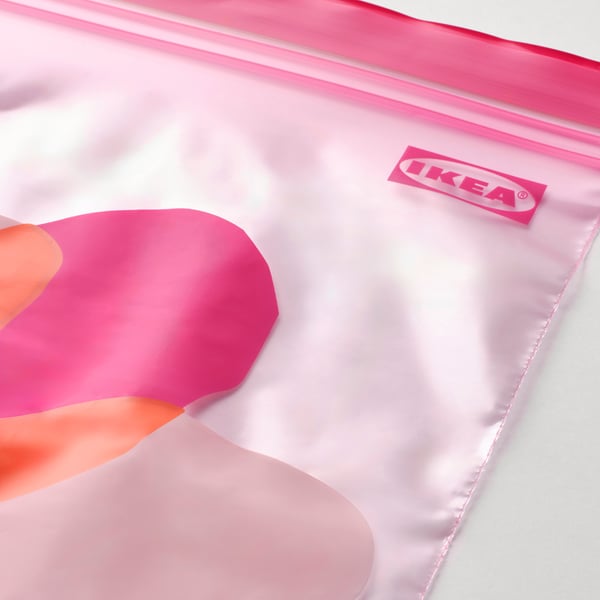 Bolsa de almacenamento IKEA rosa brillante, na súa maioría baleira, cunha man tirando a cremalleira.
