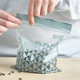 Unha persoa sela unha bolsa ikea ISTAD chea de sementes nun mostrador.