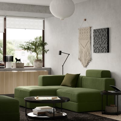 Sala de estar moderna con sofá modular verde oliva, mesa de café negra, lámpada colgante, arte de parede e planta en pota.