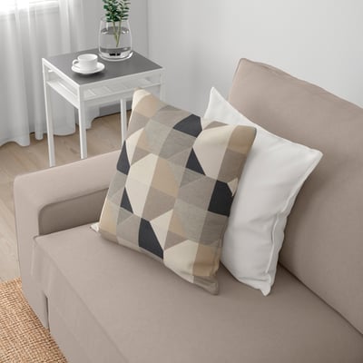 Sofá beige con almofadas brancas e patróns, mesa lateral con set de café e planta.