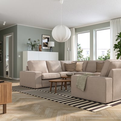Sala de estar moderna con sofá KIVIK en beige, grandes fiestras, alfombra a raias, pisos de madeira e decoración elegante.