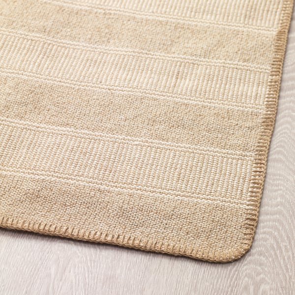 Primeiro plano da esquina da alfombra beige clara texturizada, mostrando patrón tecido e costuras duradeiras.