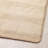 Primeiro plano da esquina da alfombra beige clara texturizada, mostrando patrón tecido e costuras duradeiras.