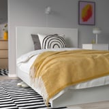 Cama con manta dourada KLIPPOXEL, almofadas xeométricas, alfombra en branco e negro, mesa de noite con lámpada, paredes grises, arte abstracta colorida e luz colgante.