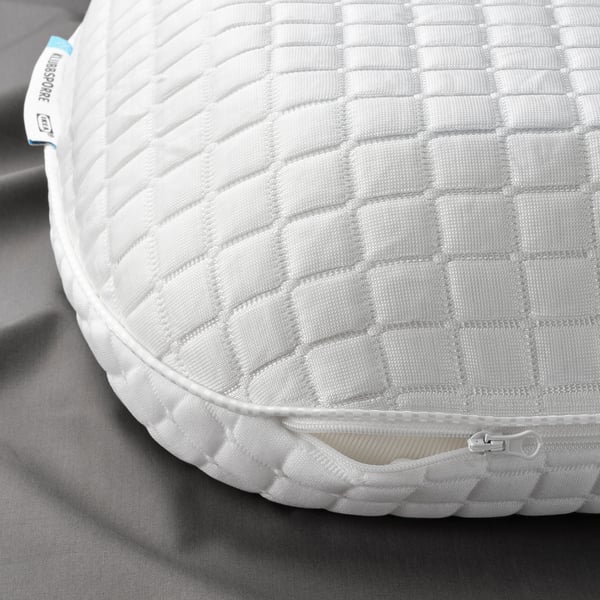 Primeiro plano de almofada ergonómica con patrín quilted, cremalleira visible e etiqueta que indica materiais de alta calidade.