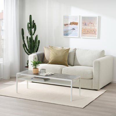 Sala de estar moderna con alfombra branca, sofá beige, mesa de café e cactus altos.