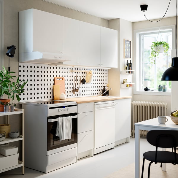 Pequena cociña branca con armarios KNOXHULT, polka dot backsplash, forno inoxidable, mesa de madeira, disposición eficiente, estantes de parede e zona de comedor.