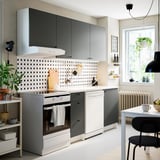 Cociña moderna con armarios grises KNOXHULT, tapa de traballo de mármore branco, electrodomésticos inoxidables, backsplash de puntos, plantas colgantes e cadeiras negras.