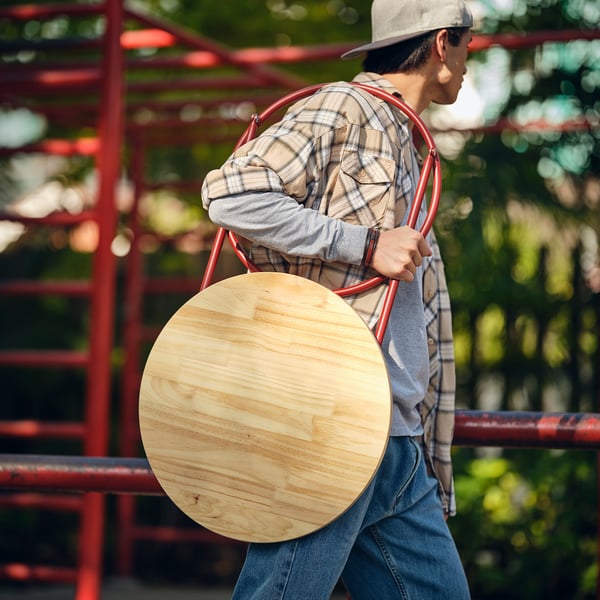 Persoa que leva a mesa lateral vermella dobrada de KOMPISHÄNG , mostrando portabilidade.