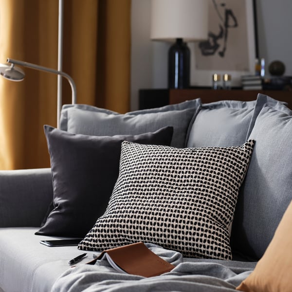 Sala de estar gris moderna con coxíns; un con patrón en branco e negro, textura suave e cremalleira.