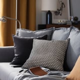 Sala de estar gris moderna con coxíns; un con patrón en branco e negro, textura suave e cremalleira.