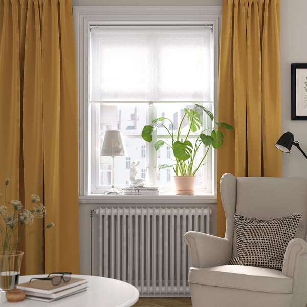 Sala de estar acolledora con cortinas de mostaza, cadeira gris, mesa de libros, planta, lámpada.
