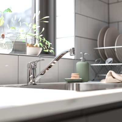 Billa de cociña cromado moderna con deseño elegante, dispensador de xabón verde e pequena planta en lavabo con baldosas grises.