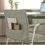 Cadeira de oficina con petos traseiros que albergan cadernos e unha nota adhesiva, ideal para un fácil acceso e organización.
