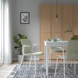 Zona de comedor moderna con paredes grises, armarios de madeira clara, mesa branca, 3 cadeiras verdes, alfombra branca / negra e luz de lámpada colgada.