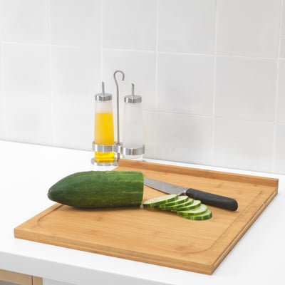 Táboa de corte de madeira con coitelo e pepino cortado; Dispensadores de aceite detrás.