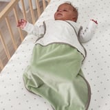 Bebé en saco de durmir branco co fondo verde, deitado nas costas no berce, brazos estendidos, ollos pechados, saco de durmir pechado.