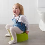 Un neno pequeno sentado nun pottyrainer LILLA verde, deseñado para adestramento no baño con base antiescorregadizante.
