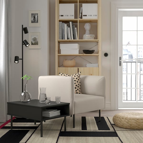 Sala de estar minimalista con sofá branco, mesa de café negra, estante alto e gran xanela.