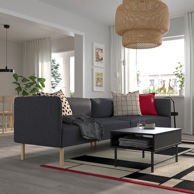 Sala de estar moderna con sofá modular gris, almofadas de lanzamento, mesa de café, lámpada colgante, plantas e imaxes enmarcadas.