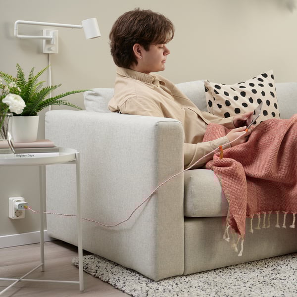 Persoa tricotando no sofá beige cun cable USB vermello LILLHULT enchufado.