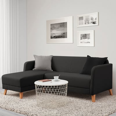 Sala de estar moderna: sofá LINANÄS negro en forma de L, almofadas grises, mesa de café redonda branca baixo a arte da parede na parede clara. Acolledor, compacto.