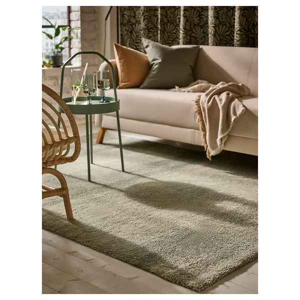 Sala de estar moderna con alfombra gris, sofá beige, cadeira de vimbio e mesa verde.