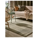 Sala de estar moderna con alfombra gris, sofá beige, cadeira de vimbio e mesa verde.