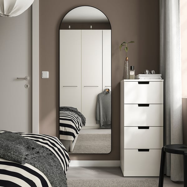 Dormitorio moderno con espello de arco LINDBYN, gran armario branco, cama con marco negro, caixóns brancos e taburete. O espello e o armario dominan o espazo.