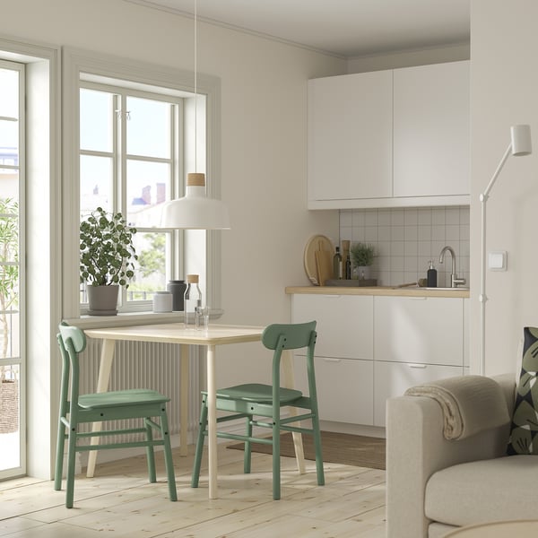 Conxunto de comedor compacto moderno con mesa branca, cadeiras verdes, cociña branca e sofá.