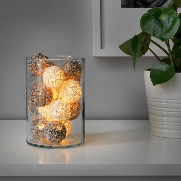 Un vaso de vidro sostén luces de corda con lámpadas de globo acesas, creando un ambiente acolledor nun andel.