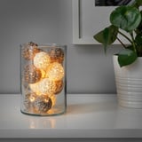 Un vaso de vidro sostén luces de corda con lámpadas de globo acesas, creando un ambiente acolledor nun andel.