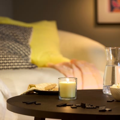 Dormitorio con vela LOTSFÅGEL na mesilla, xunto a unha jarra de auga e un bol, cunha cama acolledora ao fondo.