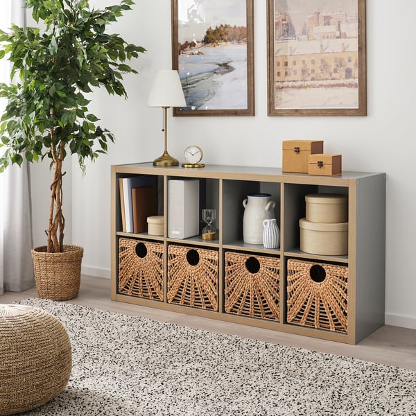 Sala de estar con cesta LUSTIGKURRE en estante kallax, lámpada, reloxo, libros, vasos. Decoración acolledora e neutra.