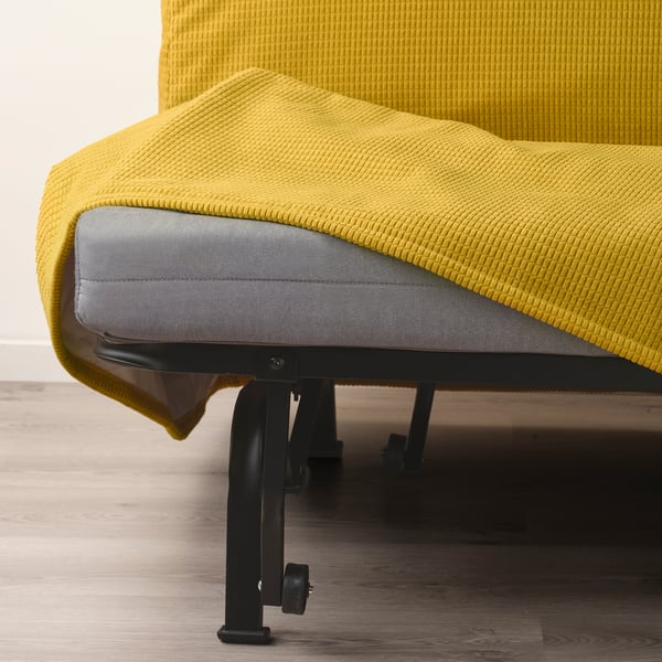 Sofá amarelo brillante con anexo de colchón gris, sostido por patas metálicas negras.