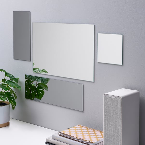 Unha configuración de parede inclúe espellos de varios tamaños conectados con cinta de dobre cara, un altofalante e planta en pota, mostrando funcionalidade de decoración do fogar.