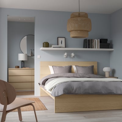 Dormitorio azul con cama MALM, roupa de cama gris, lámpada colgante, mesa lateral e estante de parede.